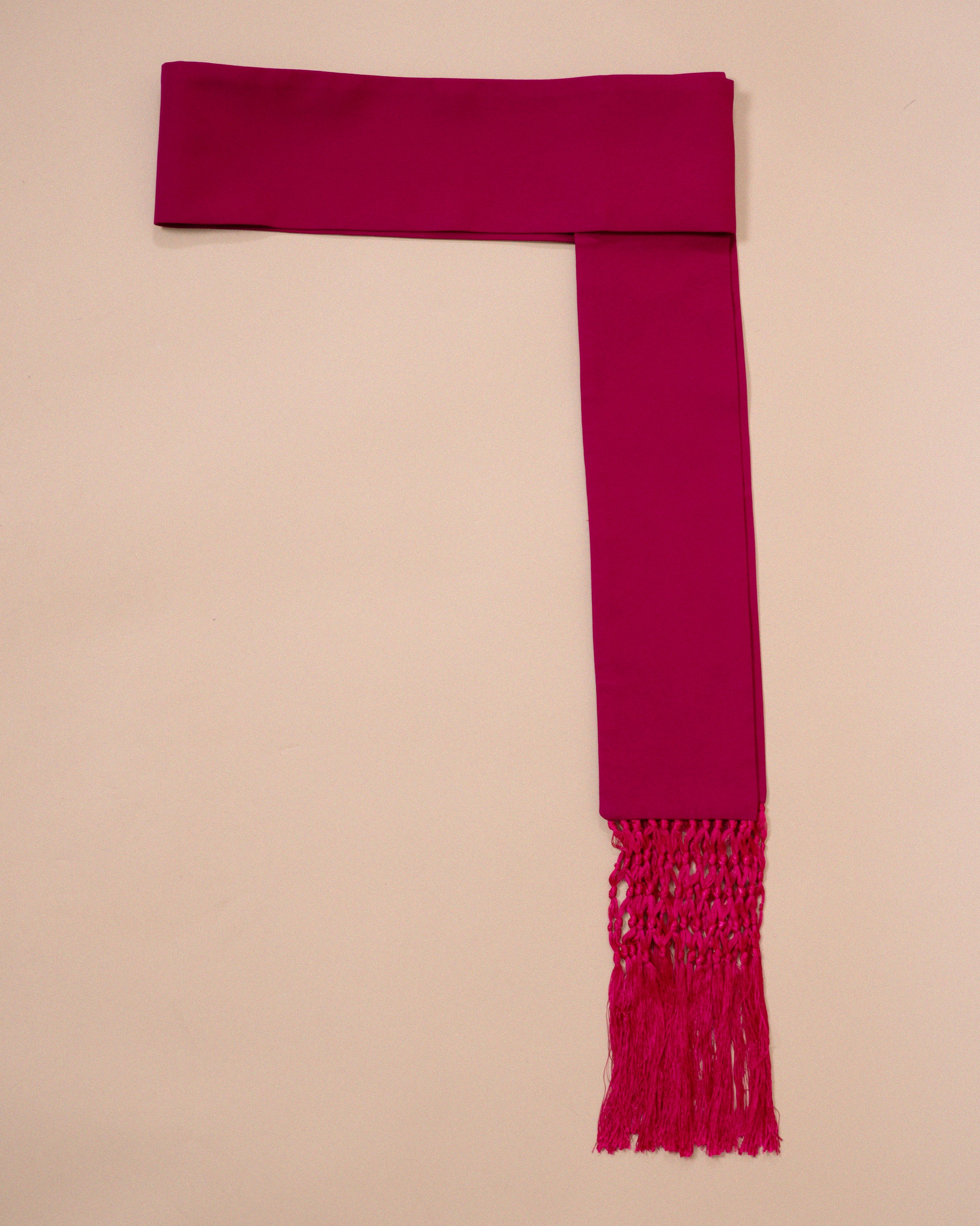 A magenta pink wool cincture with a woven fringe, laid flat on a light beige background.