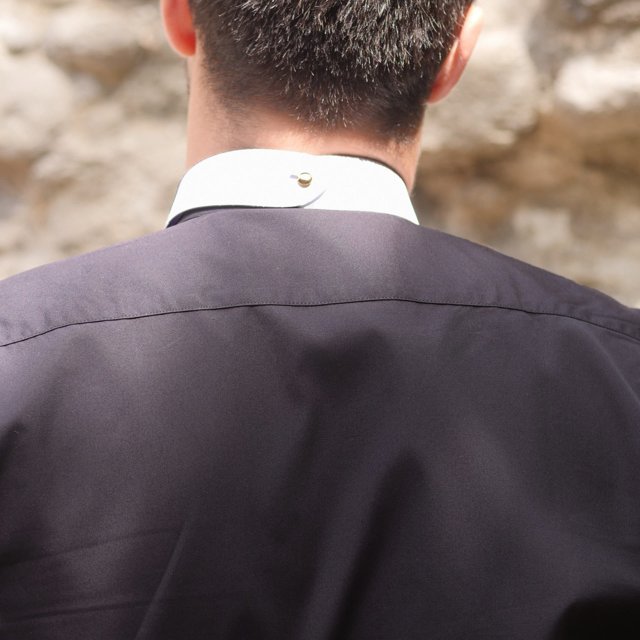 Back view of a man wearing Watts' tunic-style clergy shirt with white collar, highlighting its design and fabric in natural light.